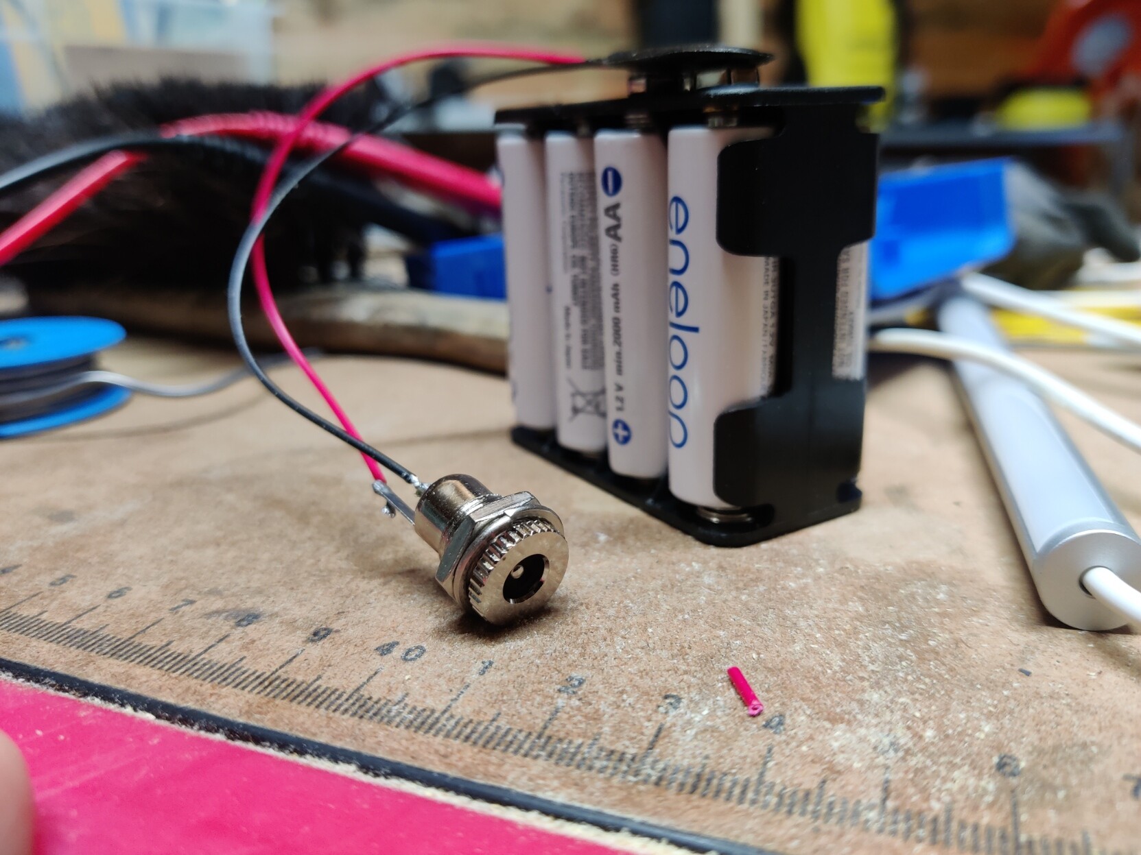 A battery housing for 4 AA batteries with a 9V connector soldered on top of it and a barrel connector soldered to the two cables coming from the 9V connector.