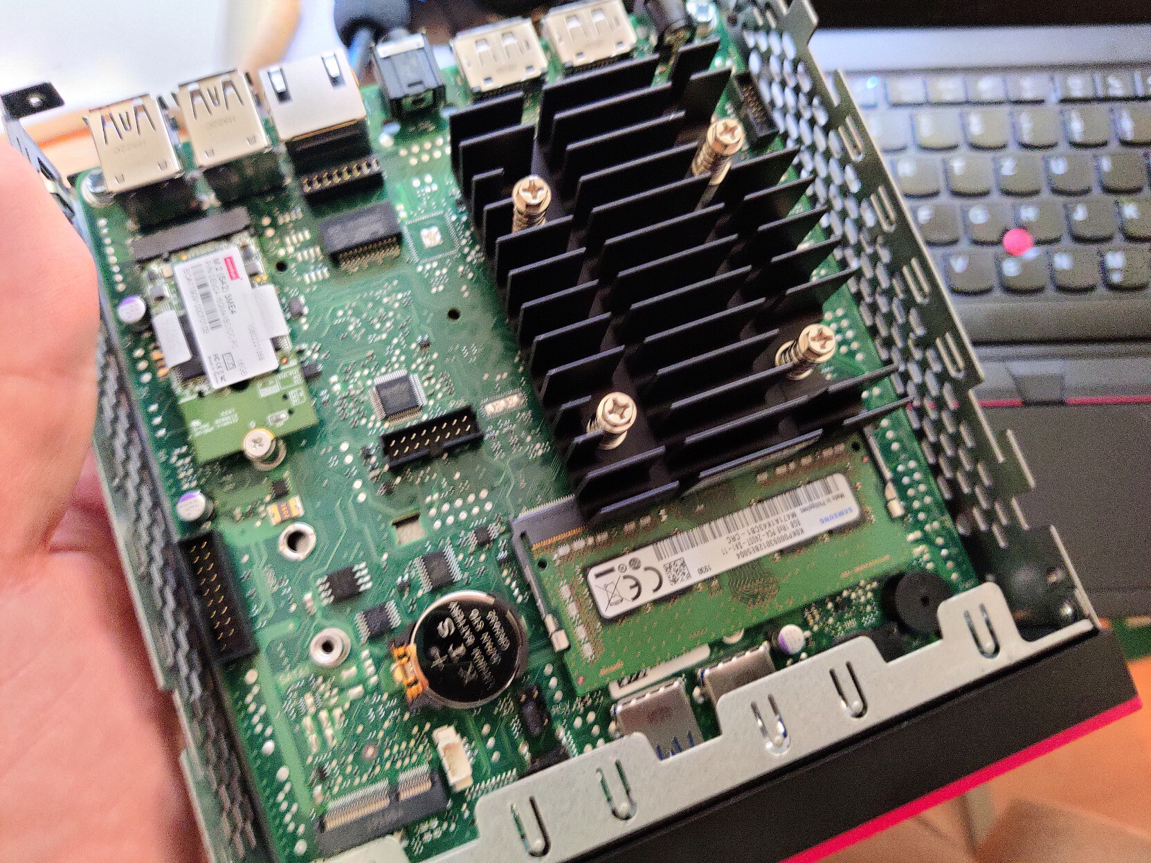 View of a disassembled small computer. The main board is visible as well as the cpu cooler, a ram dimm and an m2 SSD slot.