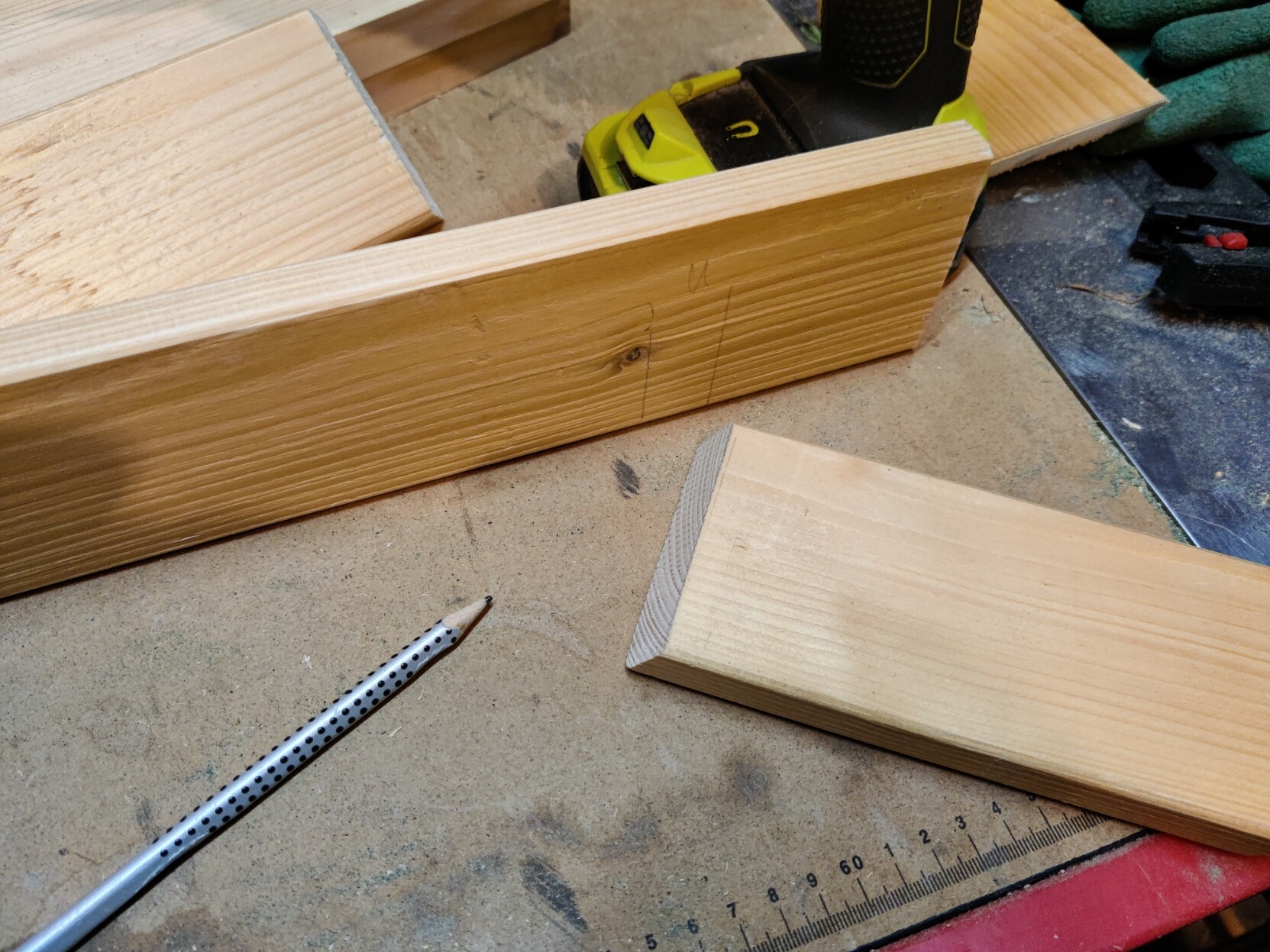 Two pieces of wood next to a pencil, the longer piece has markings where the smaller piece will be joined to. The smaller piece is already cut at an angle