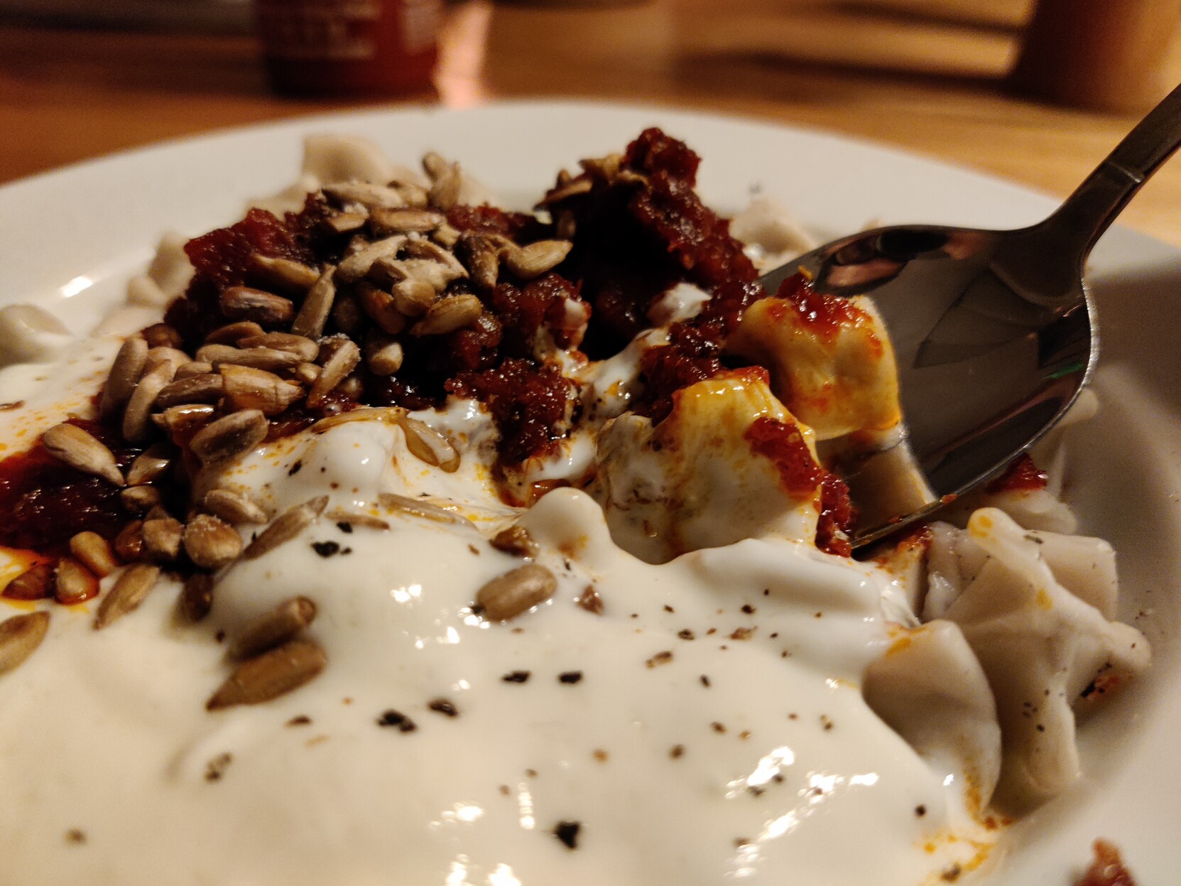 A plate of Manti with yogurt sauce, sunflower seeds and tomato sauce
