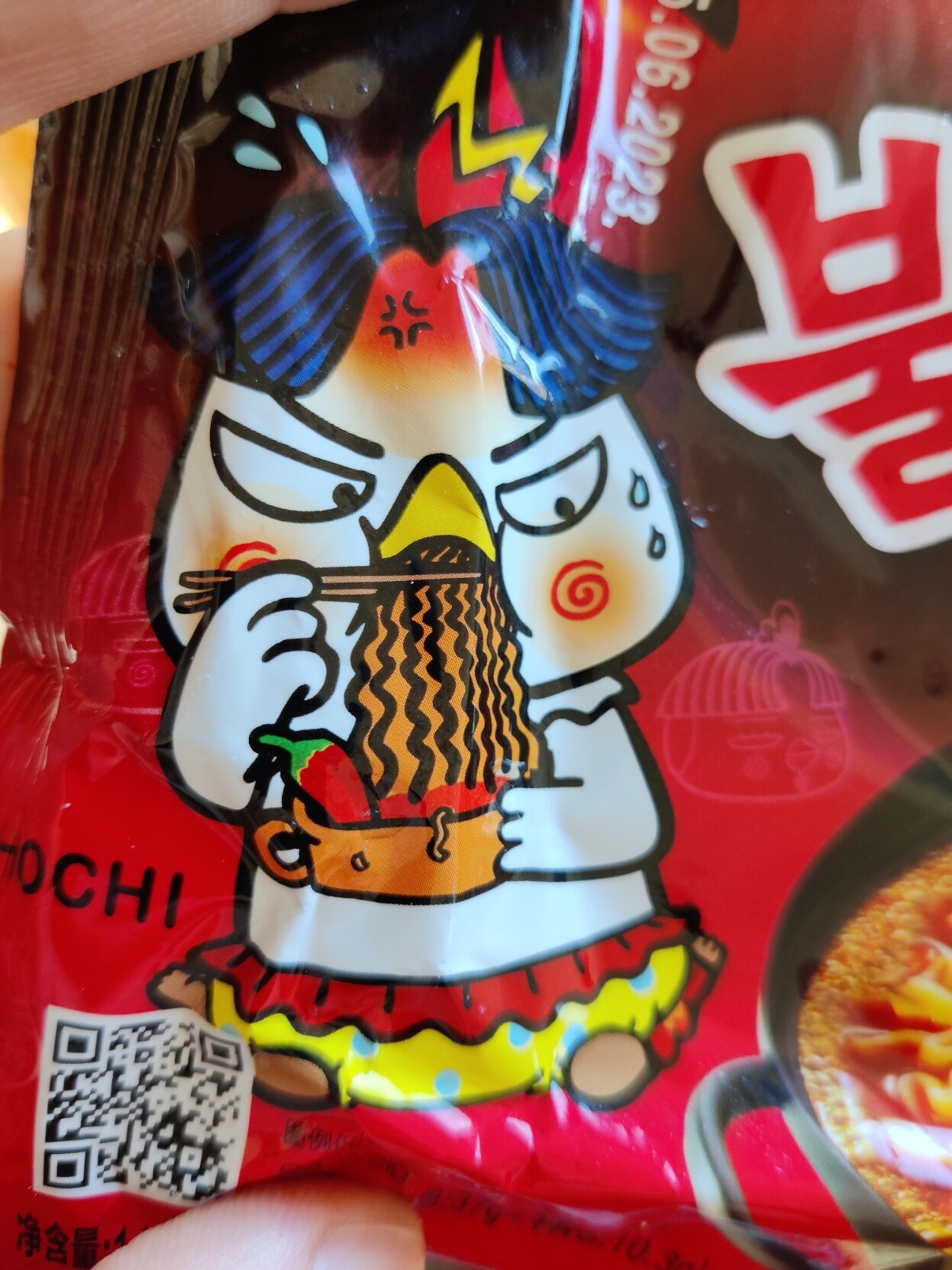 Photo of a package of Korean hot noodles, zoomed into to the chicken that eats the noodles from a pot while sweating profoundly.
