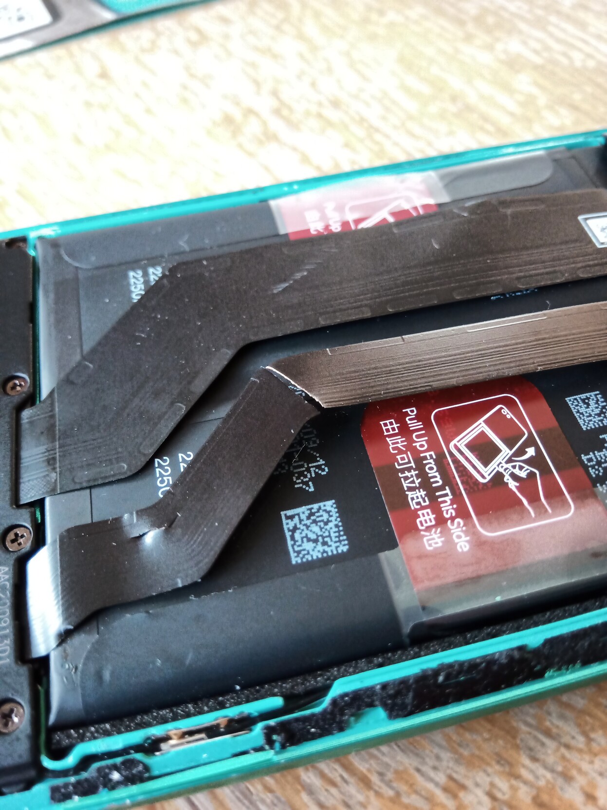 A phone with the backside open and two ribbon cables - one of them cut in the middle.