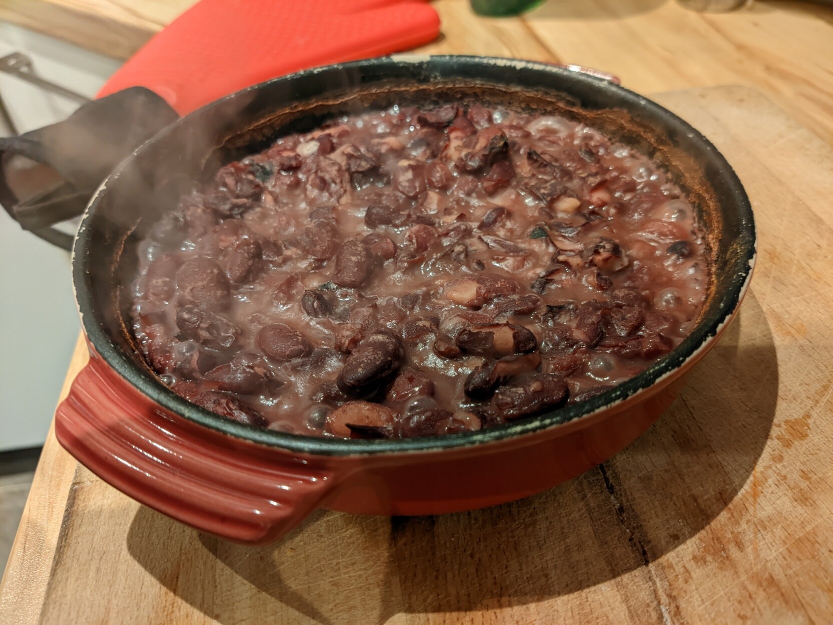A red pan with a load of red fried beans in it. It is still steaming hot and the beans started to disintegrate. It does look not at all appetizing.