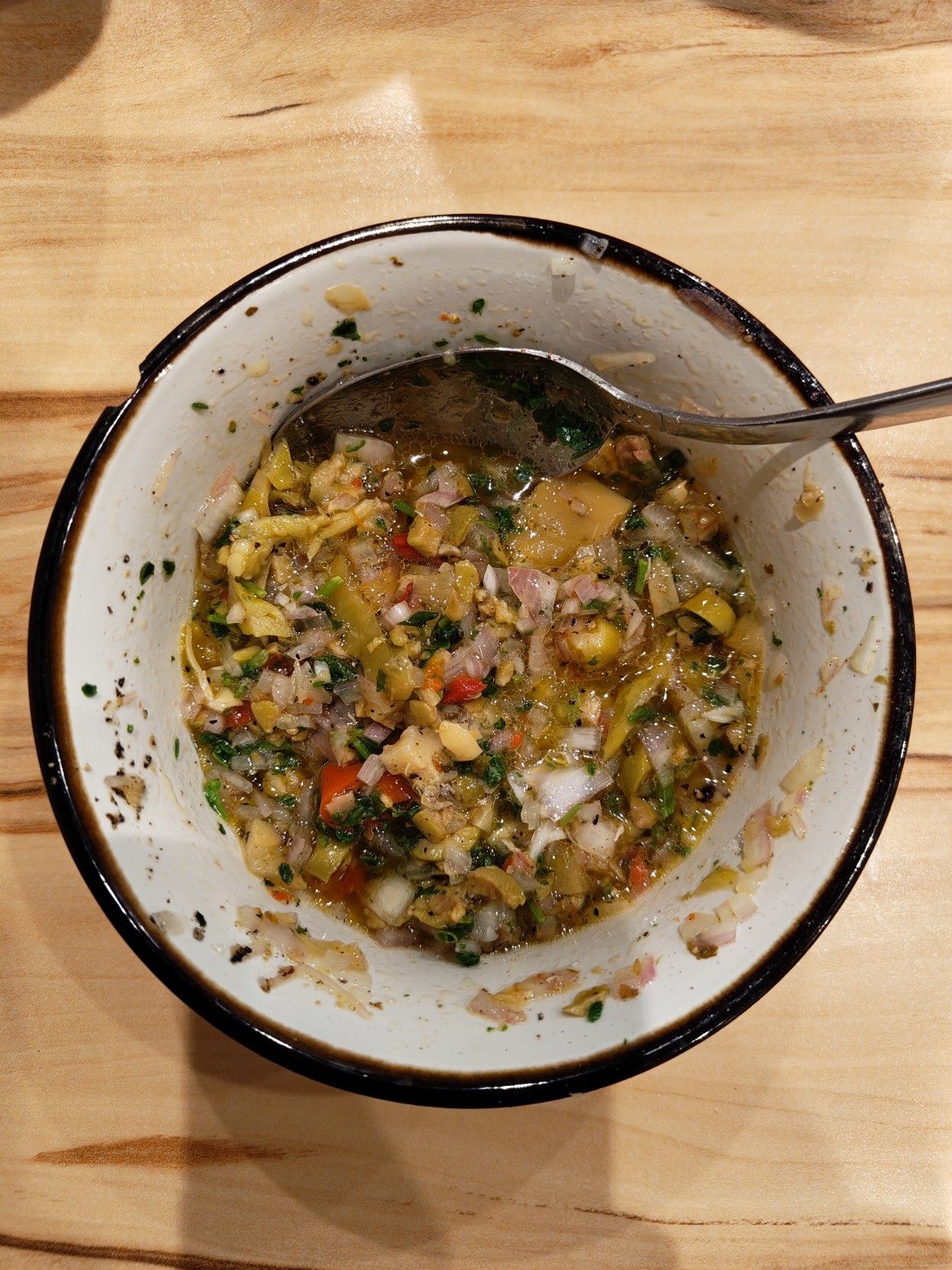 A small bowl of salad dressing with big chunks of olives, shallots and herbs in an oily base